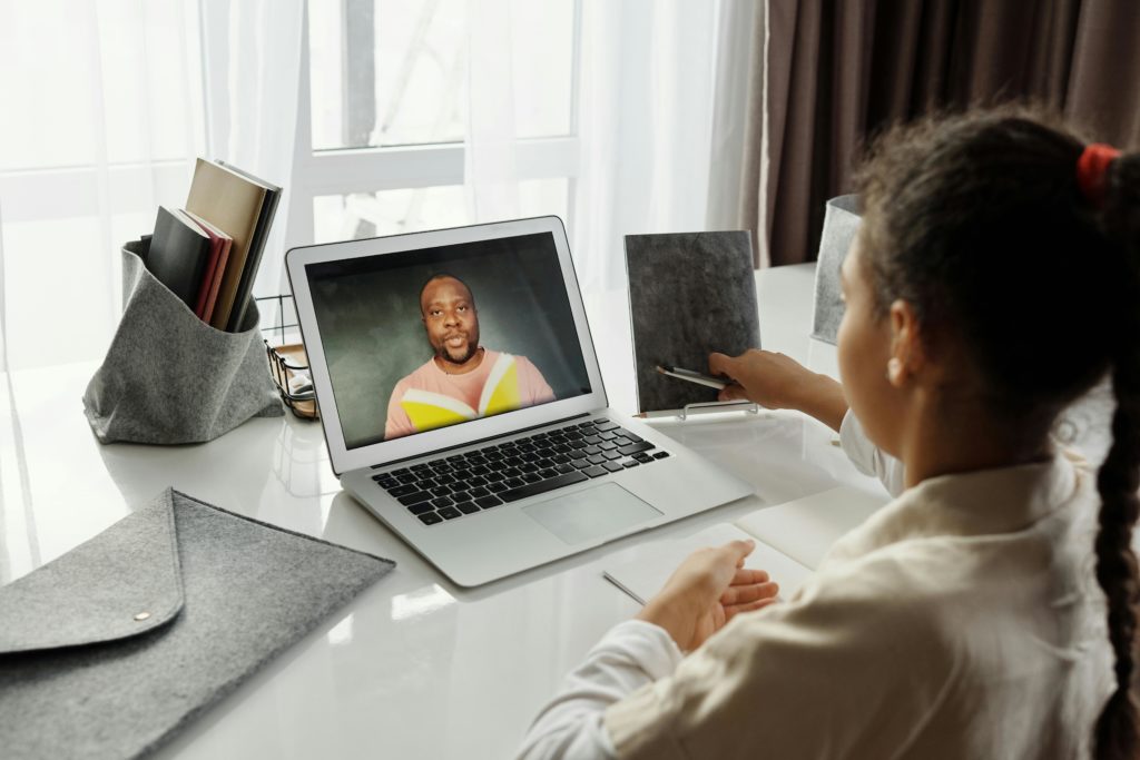 A young girl participates in an interactive online class with a teacher on a laptop, fostering education from home.